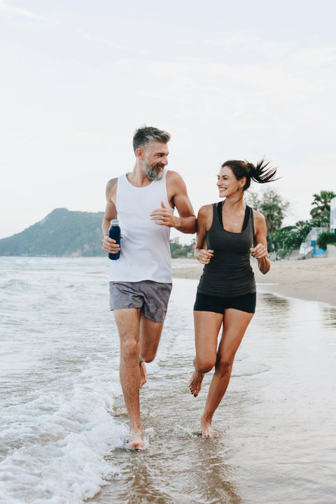a man and a woman running on the beach with healthy hair